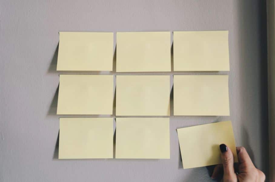 Blank post-it notes on a board and a woman's hand moving one note. 