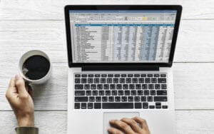 Business woman looking at a spreadsheet of data on her laptop with coffee in one hand