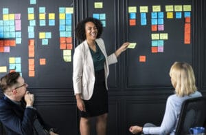 two business women and one business man setting goals for their business using post-it notes in a meeting