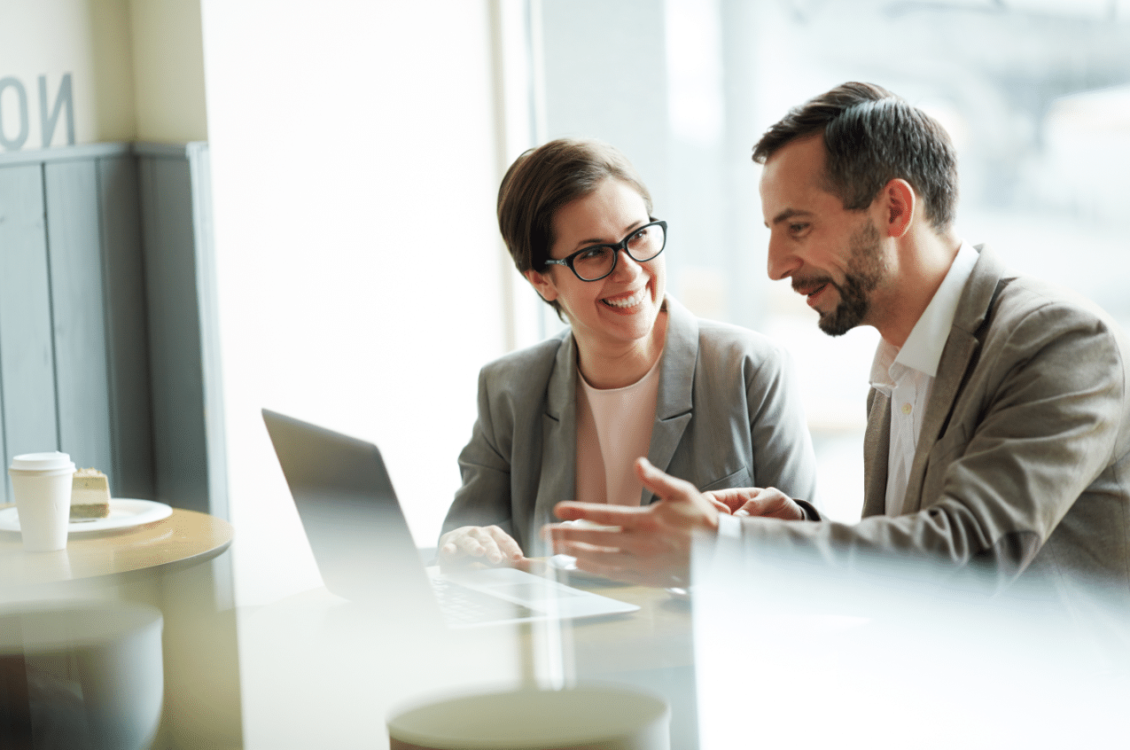 A white woman and a white man connect over a computer while sitting together at a coffee shop learning how to build a professional network